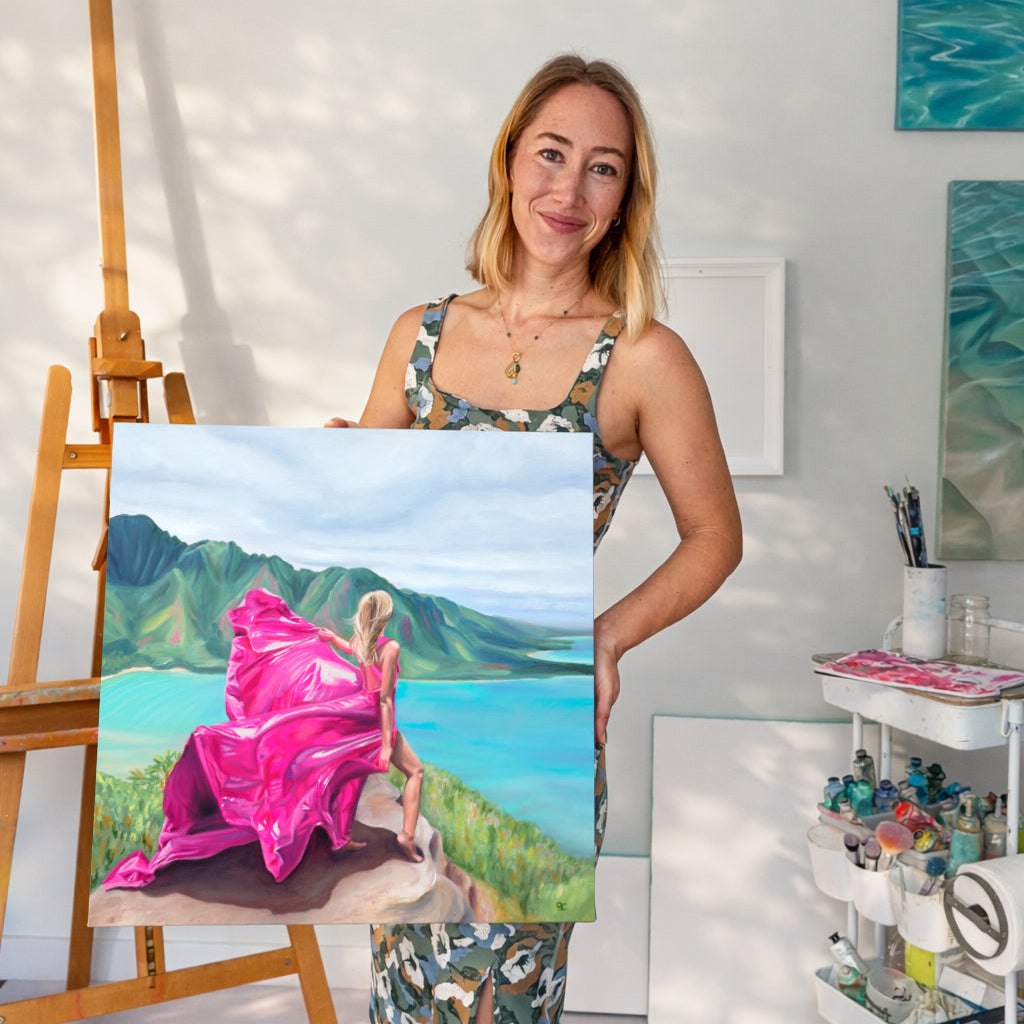 artist in an art studio holding a painting of a woman wearing a pink dress climbing a mountain